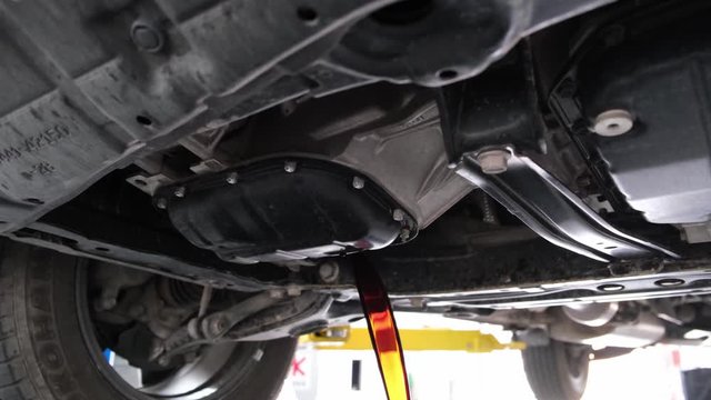 Mechanic hands draining car engine oil from undercarriage during service