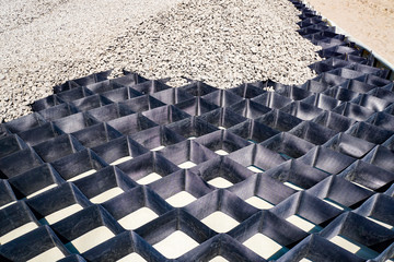 Obraz premium large black geogrid covered with gray gravel, road construction, close-up
