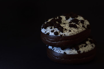 Close-up of two dark donuts with white glaze and brown spots against dark brown background with space for text