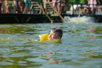 little toddler kid swimming in lake with inflatable arms aids support