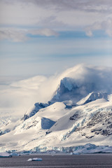 Fototapeta na wymiar Snow and ice on the mountains near the water in Antarctica, a pristine remote environment affected by global warming and climate change