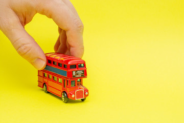 British toy double-decker red bus riding by male hand on yellow background. Concept of English language lesson and improving talking and speaking skills 
