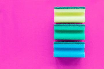 A stack of multicolored dishwashing sponges on a pink background with space for writing.