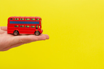 British toy double-decker red bus holding by male hand on yellow background with copy space for your text. Concept of English language lesson 