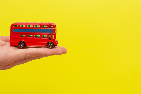 British toy double-decker red bus holding by male hand on yellow background with copy space for your text. Concept of English language lesson 