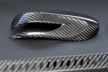 A close-up on a car exterior mirror made from carbon fiber of interwoven black and gray color from heavy-duty yarns for the production of light and durable elements in industry. Tuning body parts.
