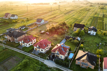 Aerial view of rural residential area with private homes between green fields at sunrise.