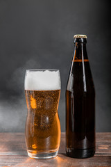 Glass and bottle with beer on a wooden table on a dark background