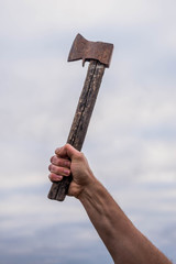 Old iron ax in hand against the sky