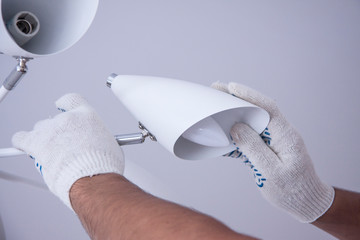 Repair of premises. Electrical work indoors. Installing a modern metal chandelier. Worker's hands in white gloves. Apartment renovation.