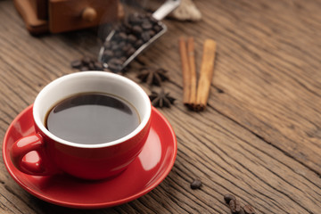 Red cup of black coffee with smoke, grinder and coffee beans on wooden table.