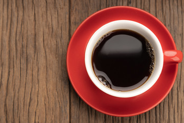 Top view of red cup of black coffee on wooden table with copy space.