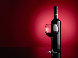 Glass and bottle of red wine on a dark red background. Copy space.