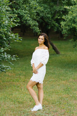 Beautiful brunette in a white dress in a clearing near the forest