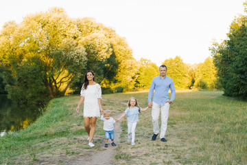 Naklejka na ściany i meble Family weekend: a beautiful young family with a small son and daughter walk outdoors