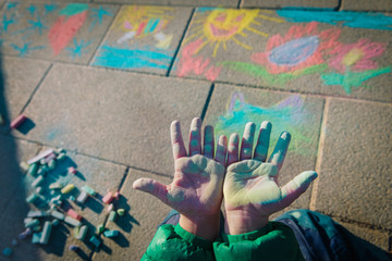 little girl showing her hands after drawing pictures on asphalt