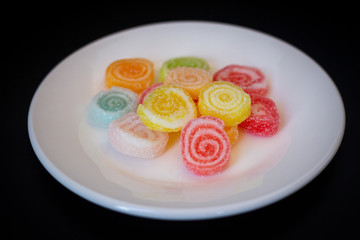 Colorful jelly rolls in white plate on black background.