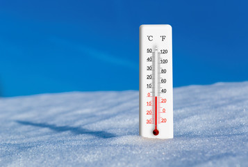 White thermometer in snow against blue sky. Thermometer display zero degrees celsius