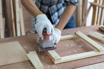 Closeup young asian carpenter polishing wooden job with sanding machine - Handyman and diy concept
