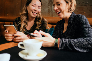 Two female friends in a cafe having coffee, smiling and chatting	