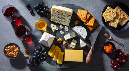 Cheese assortment on dark marble cutting board with red wine. Grey background. Top view.