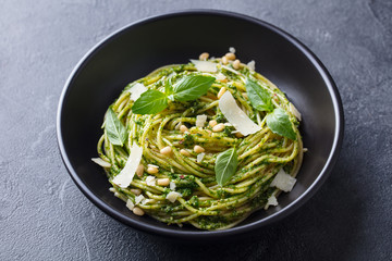 Pasta spaghetti with pesto sauce in black bowl. Grey background. Close up.