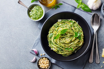 Pasta spaghetti with pesto sauce and fresh basil leaves in black bowl. Grey background. Copy space....