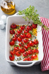 Roasted cherry tomatoes with herbs in baking dish. Grey background.