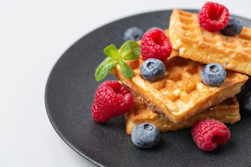 Belgian waffles with fresh berries and mint. Waffles with berries in plate on grey table. 