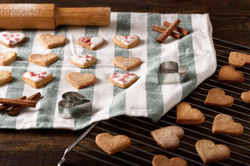 homemade cookies hearts with white icing and pastry topping on kitchen towel and metal grate