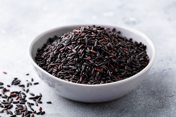 Black wild rice in a bowl. Grey stone background. Close up.