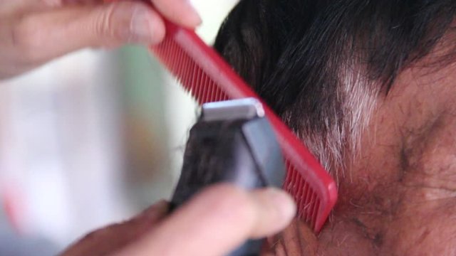 Hairdresser cutting client's hair in salon with electrical hair clipper and comb