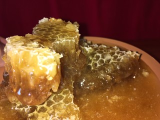 golden yellow hexagonal honeycombs in a clay brown plate on a wooden background