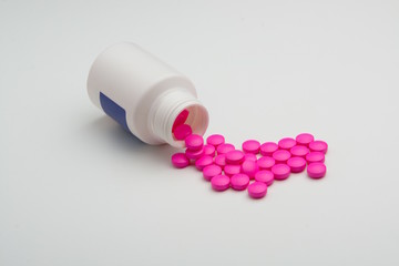 Pink medicine pills spilled from white little close up medical bottle