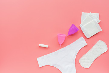 Menstrual cup with bag, hygienic pads, tampon, white panties on pink background. Alternative feminine hygiene product during the period. Women health concept.