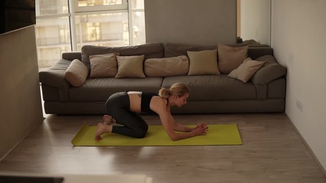 Blonde sexy slim fit woman performing correct head stand asana and gently raises legs and come back on yoga mat beauty practice. Strong hand muscular lady. Bright living room