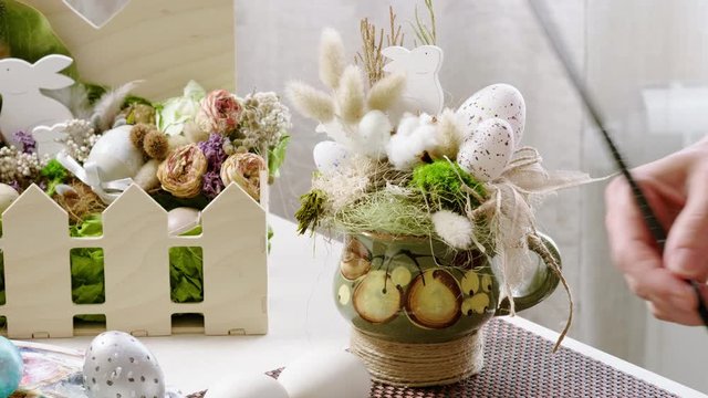 Tradition of Easter holidays. Closeup of colored eggs, wooden rabbit and flowers in basket on table at home. 4K