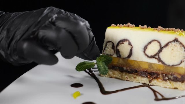 Final touches in cooking. Preparation proccess in dessert cooking. Chef hands in black gloves adding mint leaves to dish on black background. Slow motion. Full hd