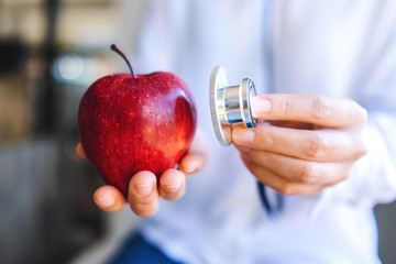 Closeup image of a doctor using stethoscope to examine a red apple