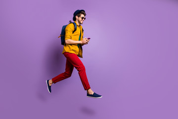 Plakat Full size profile side photo of positive guy jump use cellphone search online shopping blogs run after discounts wear blue bag hat yellow shirt red pants isolated violet color background