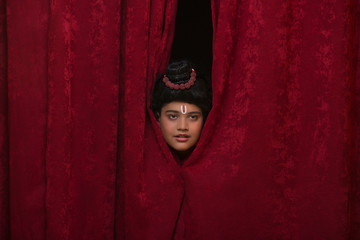 child dressed up as lord ram peeking out of curtains