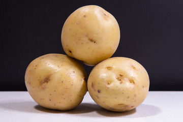 Three fresh yellow potatoes stacked on each other. Isolated potatoes in front of black background on white chopping board.