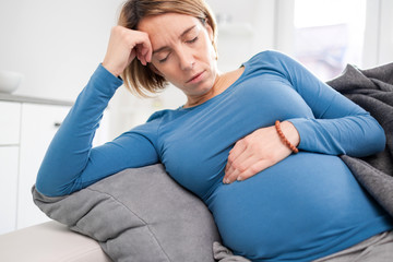 Pregnant tired exhausted woman with stomach and head issues at home on a couch, being sick.