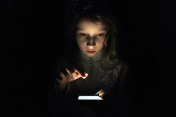 Child girl with a phone in the dark. A child clicks on the screen of a smartphone.