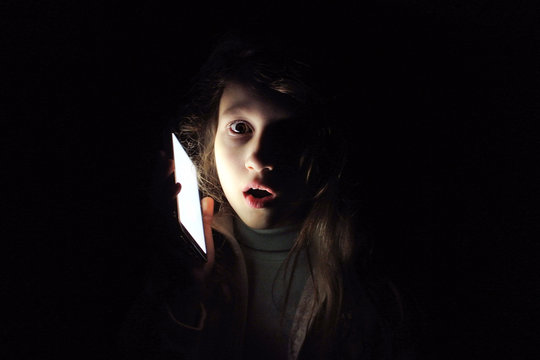 Child girl with a phone in the dark. Frightened child calls to mother: power outage.