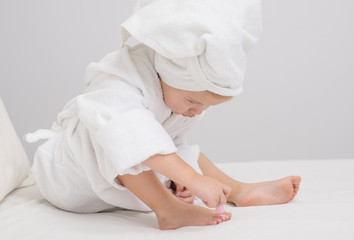 Little cute girl with a towel on her head does a manicure in her bedroom.