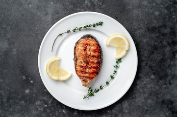 Grilled salmon steak in a white plate with spices on a stone background