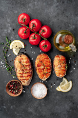 Three grilled salmon steaks with spices, lemon and tomatoes on a stone background