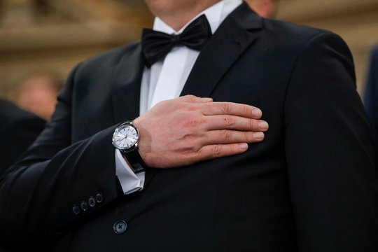 Details with a man in tuxedo holding his hand on his hearth while hearing the national anthem.