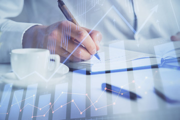 Double exposure of man's hands writing notes of stock market with forex chart.